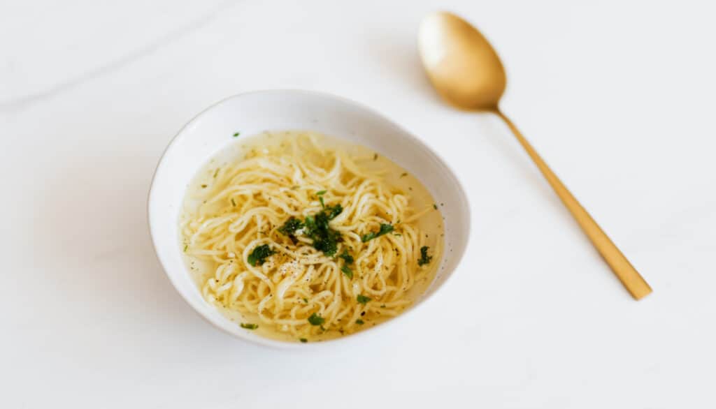 bowl of chicken noodle soup with gold spoon