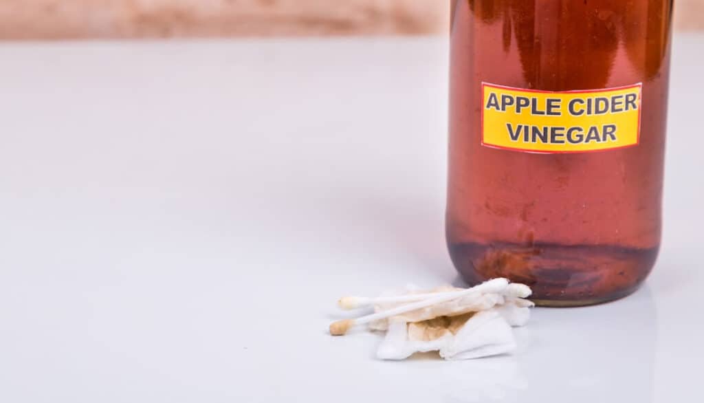 bottle of apple cider vinegar with q-tips and cotton pads